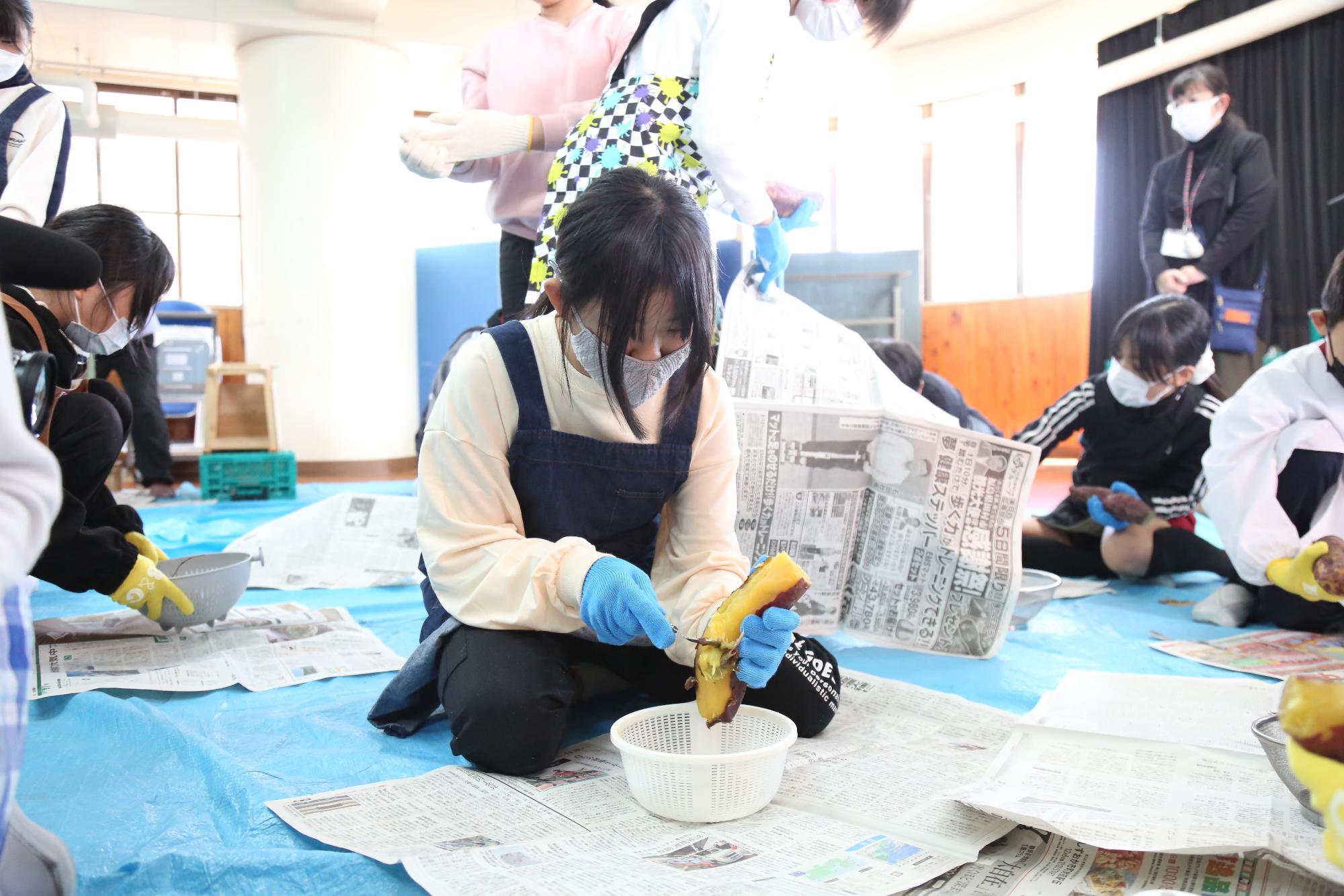 蒸かしたサツマイモの皮をむく児童