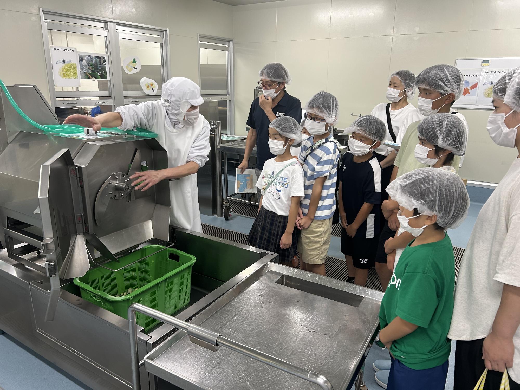 スライサーできゅうりのカットを見学している児童と保護者