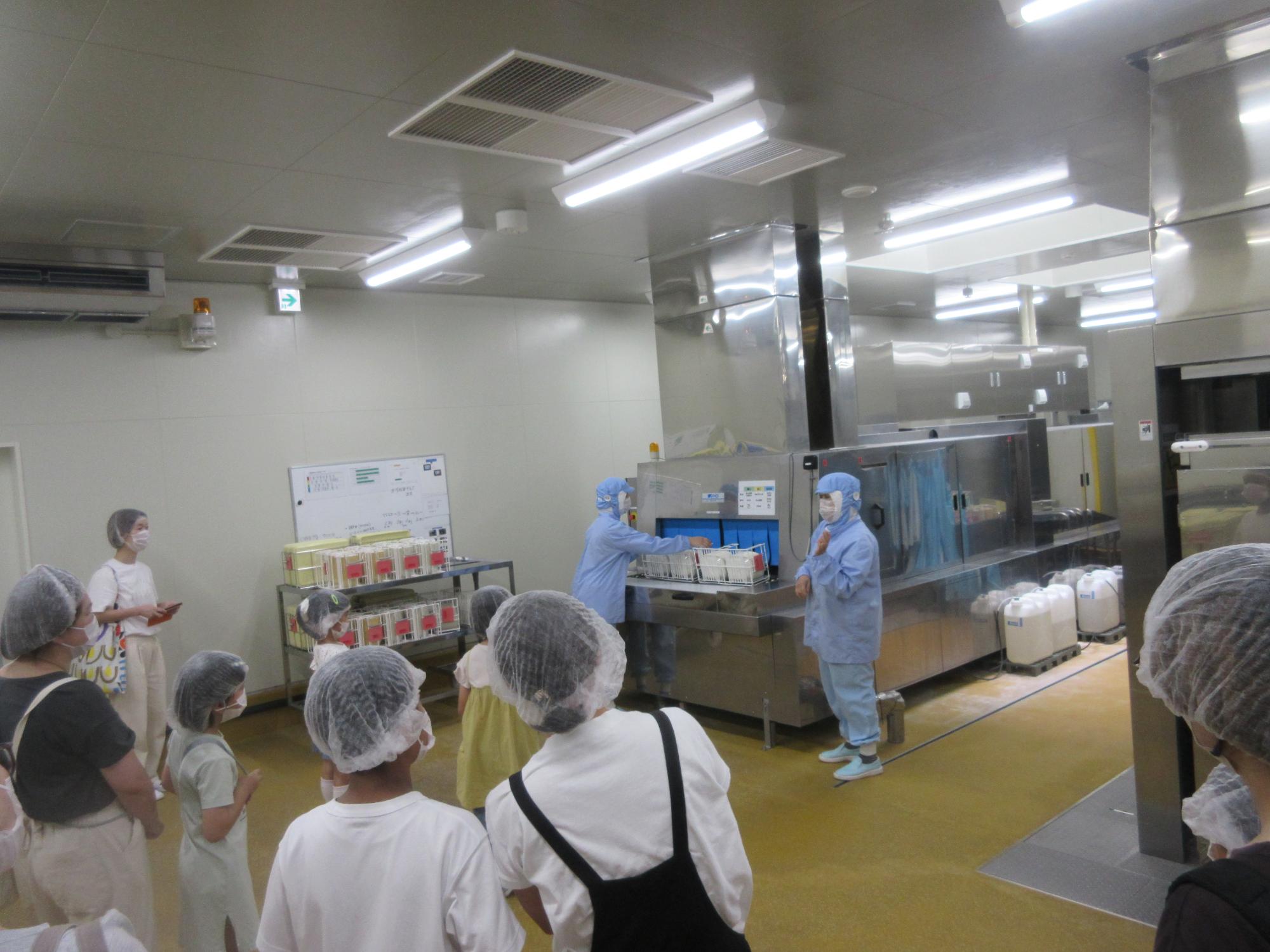 食器洗浄機へ食器を投入する様子を見学する児童
